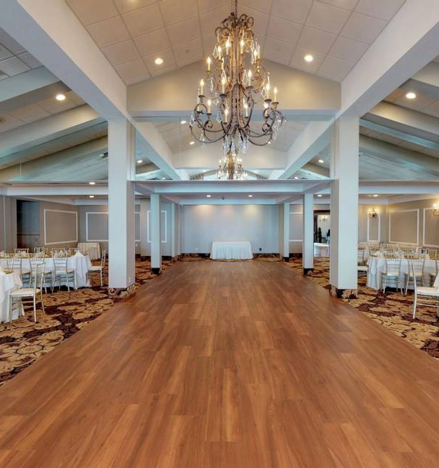 This image shows an elegant banquet hall with chandeliers, a wooden floor, and set dining tables on either side, ready for an event.