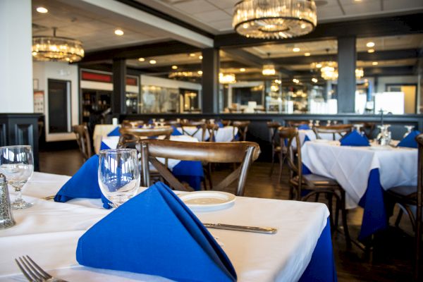 The image shows a restaurant interior with tables set with blue napkins, glasses, and plates, under elegant chandeliers.