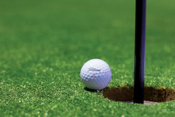 A close-up image of a golf ball resting right next to the hole on a golf green, with part of the flagstick visible in the hole.