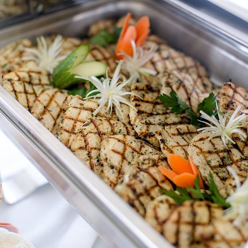 The image shows a buffet tray with grilled fish fillets, garnished with vegetables and herbs, ready to be served.