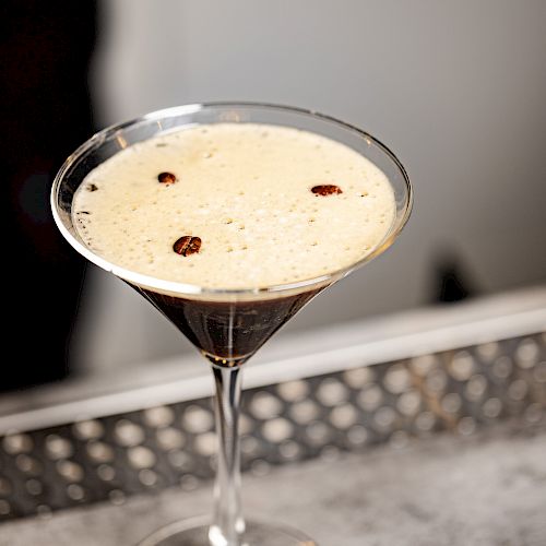 A martini glass filled with a creamy cocktail, garnished with three coffee beans, placed on a countertop.