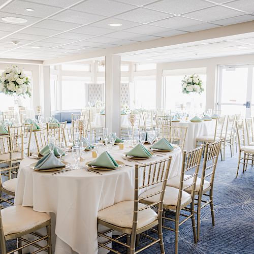 The image shows an elegantly set dining area with round tables, white tablecloths, and green napkins, decorated with large floral centerpieces.