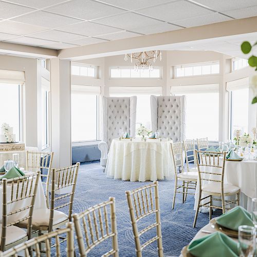 A beautifully decorated banquet hall with green and white accents, elegant chairs, round tables, and large floral arrangements.