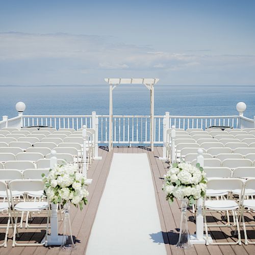 An outdoor wedding setup with rows of white chairs facing an altar overlooking the ocean, with flower arrangements along the aisle.