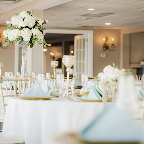 A beautifully decorated venue with elegantly set tables adorned with white flowers in tall vases and neatly folded blue napkins.