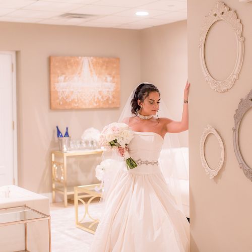 The image shows a bride in a wedding gown holding a bouquet, standing in a decorated room with empty picture frames and a mannequin in the background.