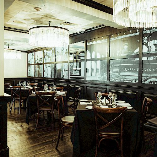 A sophisticated restaurant with chandeliers, framed black-and-white photos on the walls, and tables set for dining with dishes and glasses, ending the sentence.