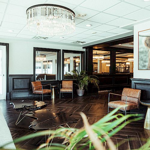 A modern waiting area with leather chairs, plants, a chandelier, and a large art piece of a highland cow on the wall.